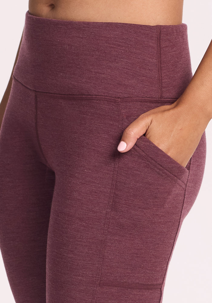 A person wearing Woolx Frost Duralite® Leggings in Grape Harvest Melange is shown from the waist down, featuring high-waisted winter leggings with a side pocket and one hand resting inside the pocket.