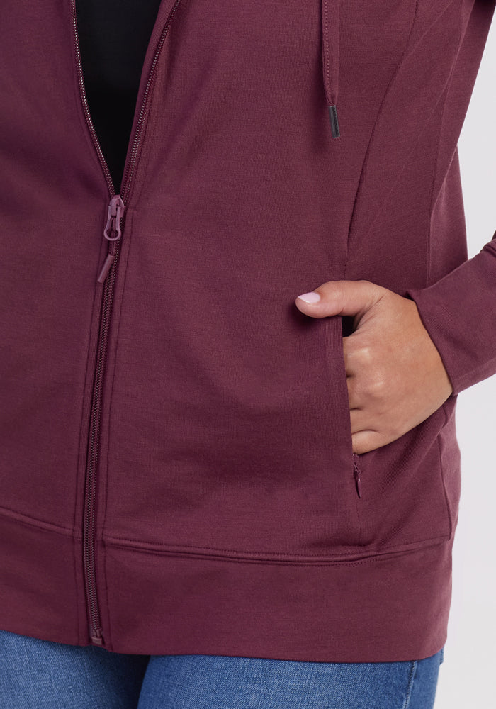 Someone wearing the Woolx Ryann Hoodie in Grape Harvest, with their right hand partially in the front pocket and paired with blue jeans. The image is cropped to show only the torso and upper legs.