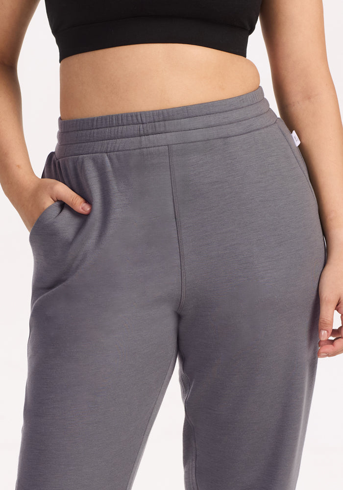 A person wearing Woolx Parker Sweatpants in Arctic Dusk and a black crop top stands with one hand in their pocket against a plain background.