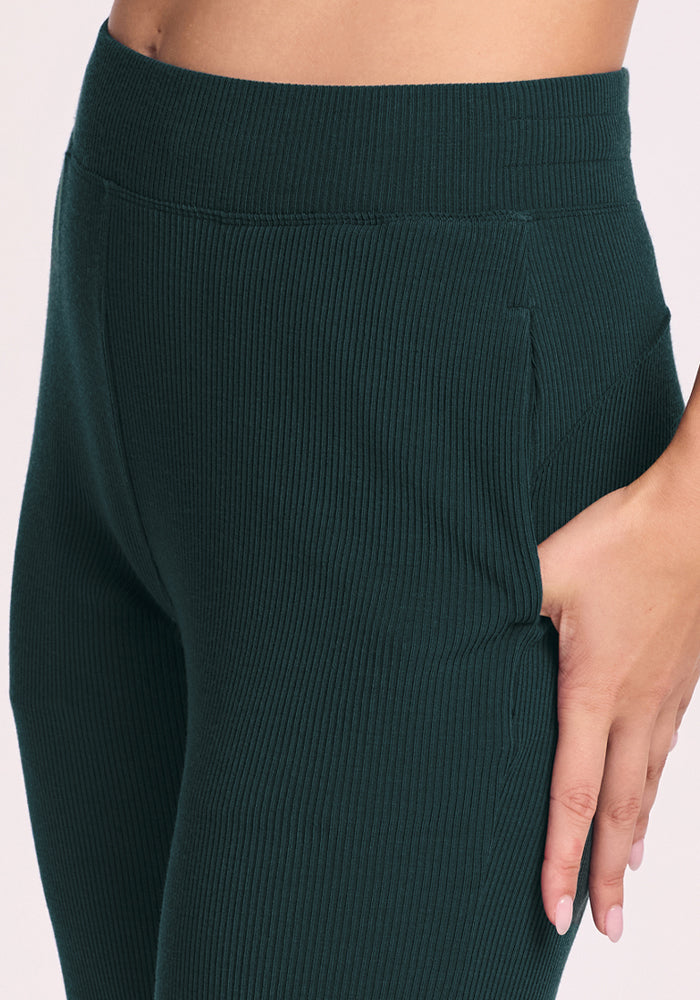 Close-up of a person wearing Woolx Luca Ribbed Pants in Deep Timber, with one hand in the side pocket. Only the waist, hip, and upper leg area are visible.
