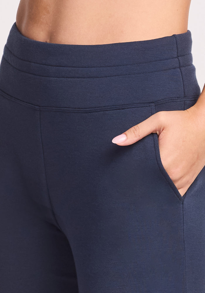 Close-up of a person wearing Woolx Willa Joggers in Deep Navy, high-waisted with one hand in a side pocket. The fit and casual style is highlighted from waist to mid-thigh.