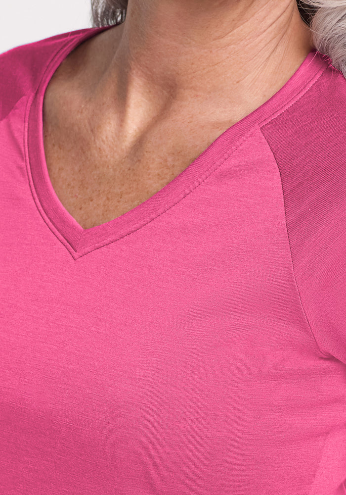 Close-up of a person wearing the Woolx Mia V Neck in Raspberry Fizz, showing its bright pink color, V-neckline, moisture-wicking Merino wool fabric, and the upper chest area. Light skin and gray hair are also visible.