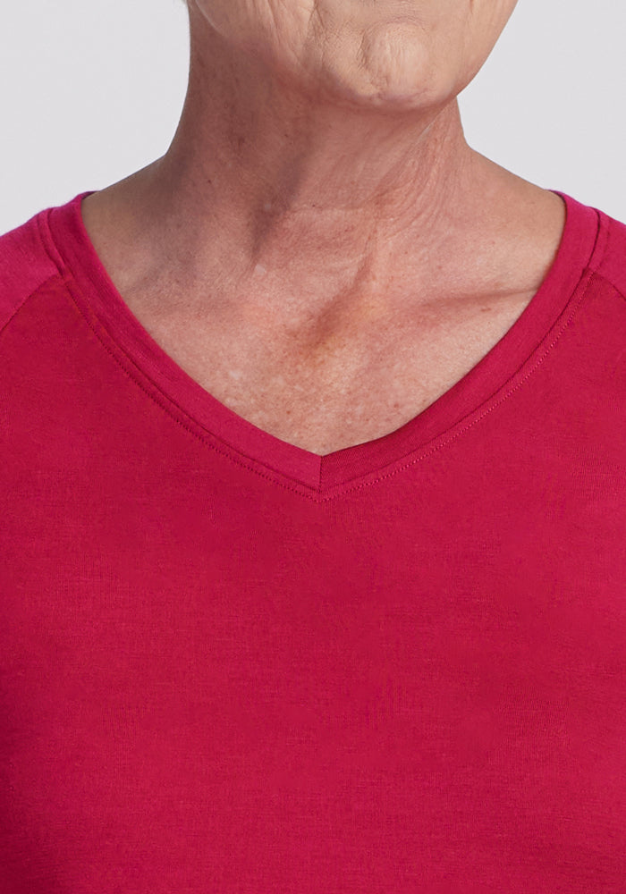 A close-up of an older person's lower face, neck, and upper chest wearing the Woolx Mia V Neck in Poppy Spark. The background is plain and light-colored.