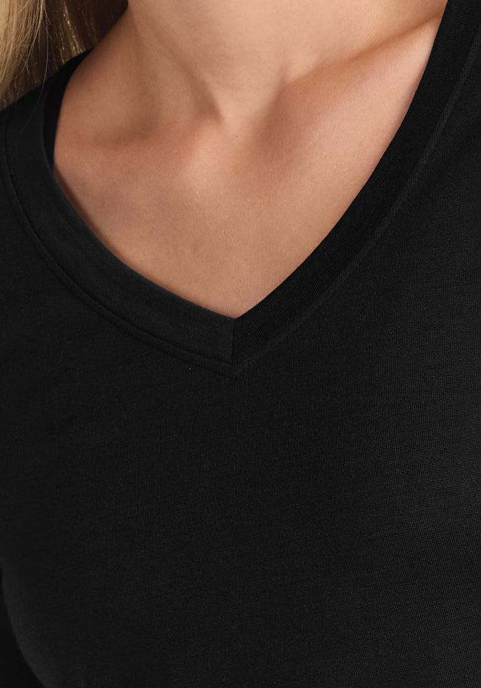 Close-up of a person wearing the Woolx Lily V Neck Lounge Top in black, highlighting the V-neckline and shoulder. Light skin and blonde hair are visible—perfect travel sleepwear for comfort and relief from night sweats.