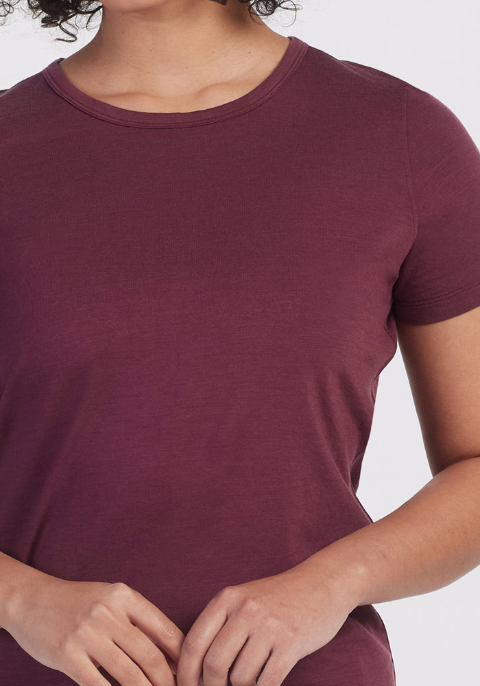 A person wears the Woolx Liza Crew Neck Tee in Grape Harvest, short-sleeved and lightweight, standing against a plain light background with only the upper torso visible and hands loosely clasped in front.