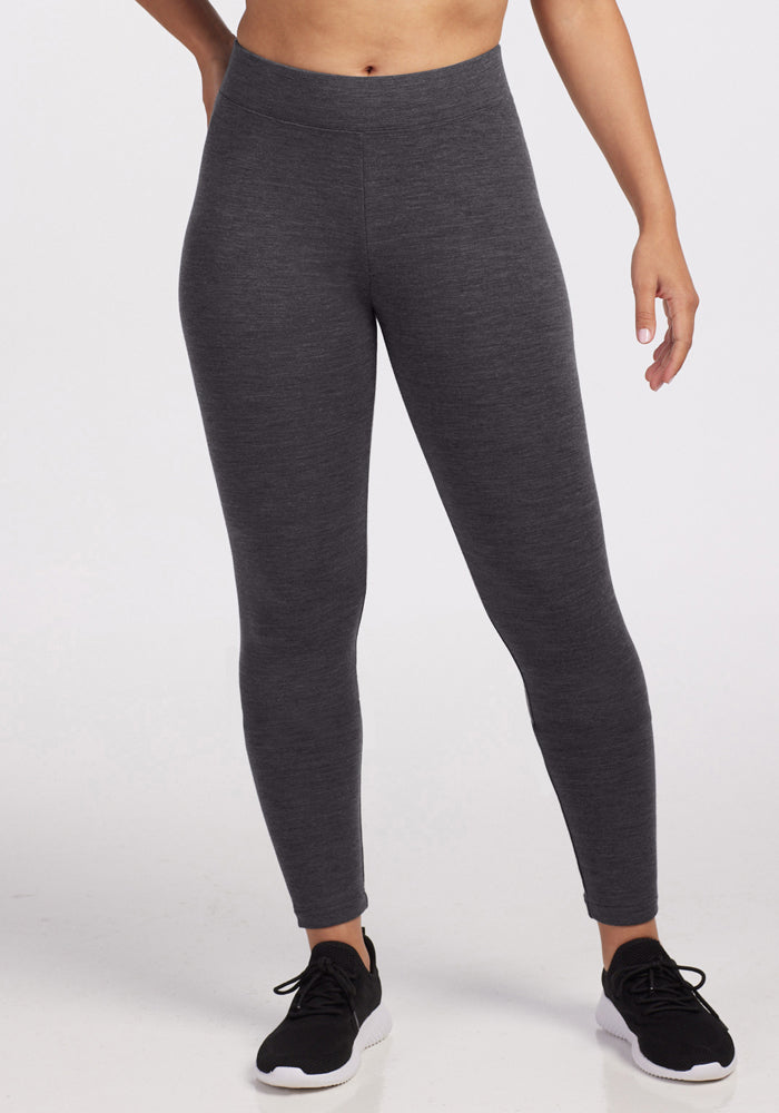 Model in Woolx Stella Tall - Cinder Melange leggings and black sneakers, shown shoulders-down on plain white.