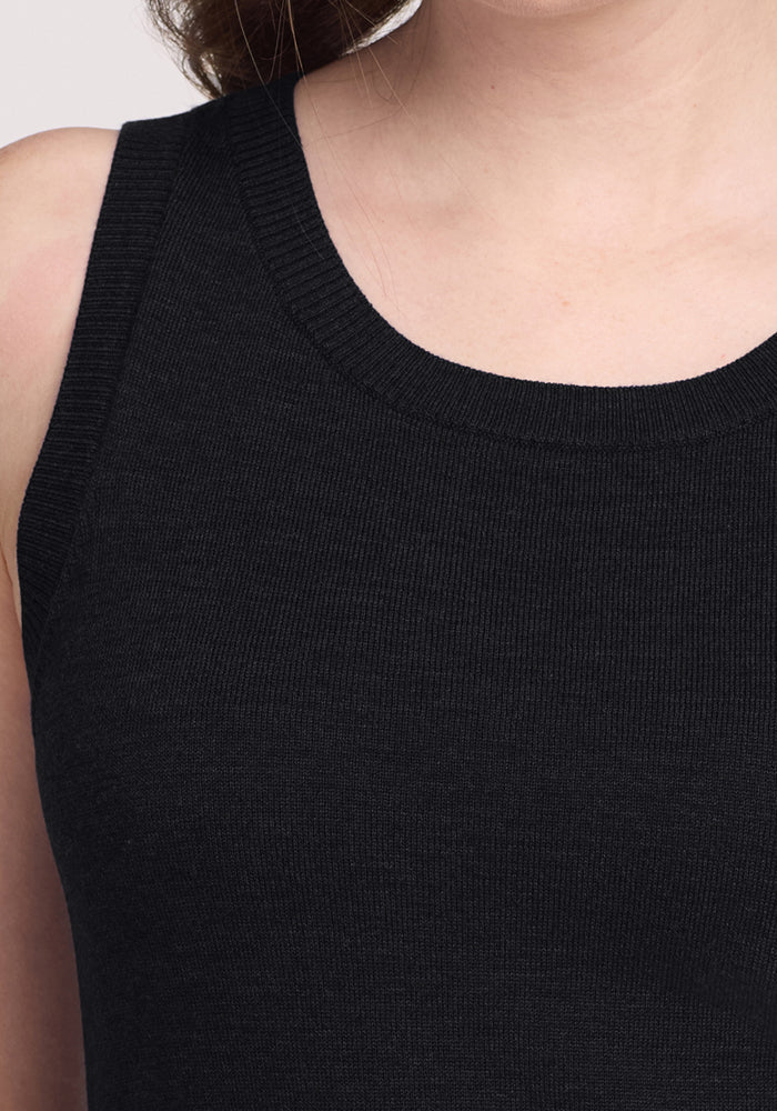 Close-up of a person wearing the Woolx Chessy Tank Top in black, focusing on the neckline, shoulders, and upper chest. The face is partially visible, emphasizing this versatile merino wool layering piece.