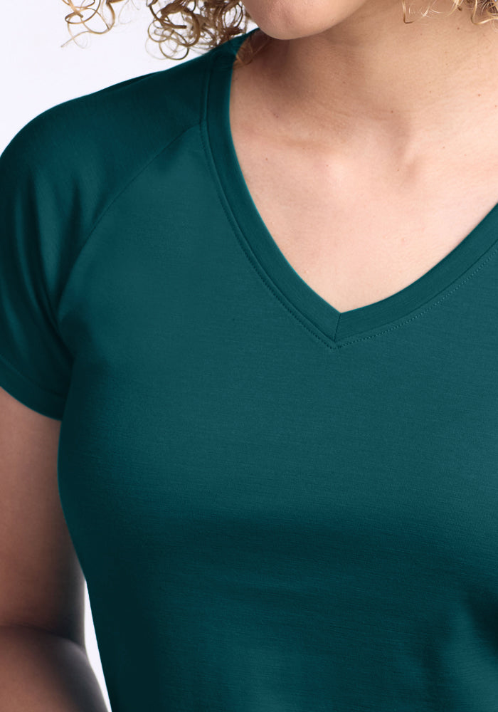 A close-up of a person wearing the Woolx Mia V Neck in Riverbank Green, showing the upper torso, part of an arm, and neck with curly hair partially visible.