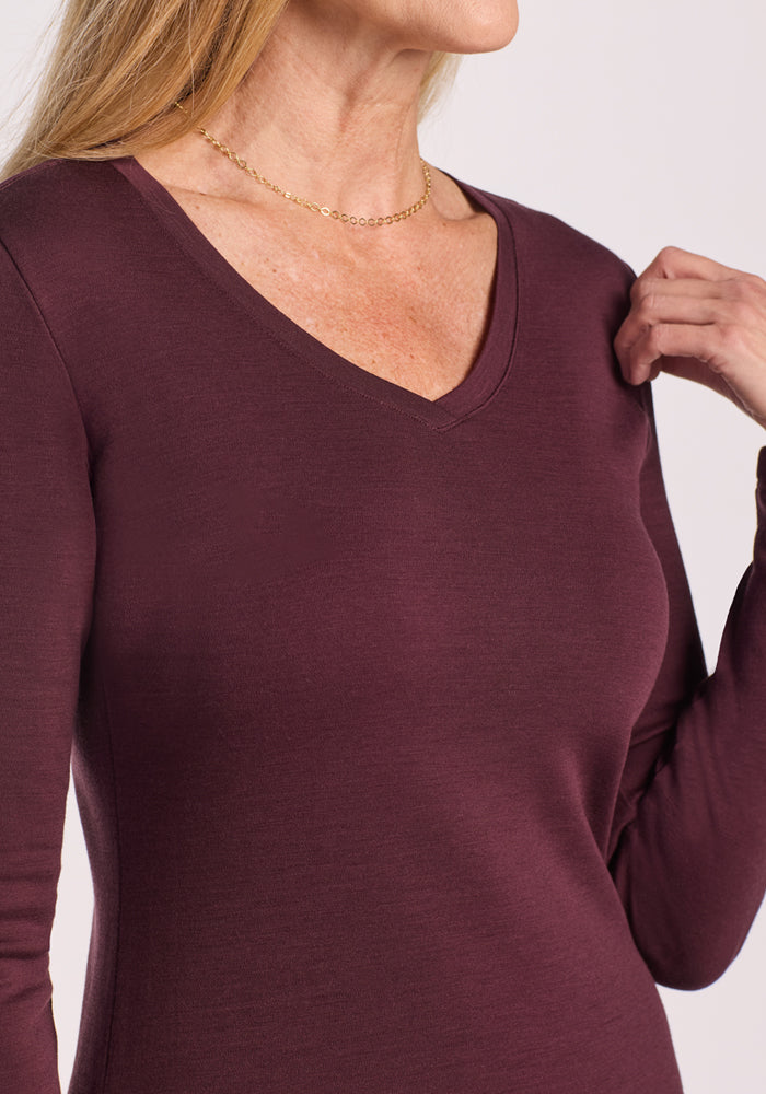 A woman wears the Woolx Eva Tunic in Chocolate Fig, a warm Merino wool piece with long sleeves, paired with a delicate gold necklace. Her hand is near her shoulder and her face is partially out of the frame.