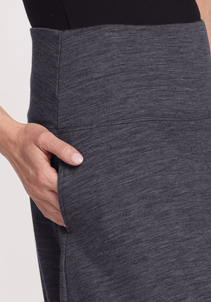 A close-up of a person wearing the Woolx Marilyn Flowy Midi Skirt in Cinder Melange, featuring a high-waisted A-line fit and side pocket, paired with a black top.