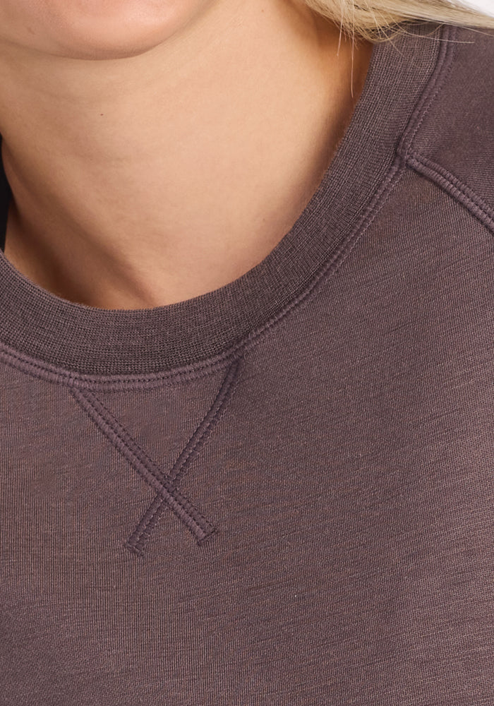 Close-up of a woman's neck and shoulders wearing the Woolx Bailey Crewneck Sweatshirt in Plum Truffle, showing stitching near the collar. Part of her chin and hair are also visible.