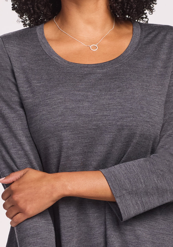 A woman wearing the Woolx Rissa A Line Dress in Cinder Melange crosses her arms. The heather gray dress is ideal for fall and winter layering. She also wears a delicate silver circular pendant necklace, with her head partially out of frame.