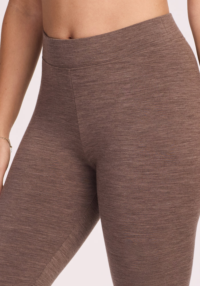 A close-up of a person wearing Woolx Stella Leggings in Simply Taupe, highlighting the high-waisted, Merino wool design at the waist and upper legs. The left arm with a delicate bracelet is also partially visible.