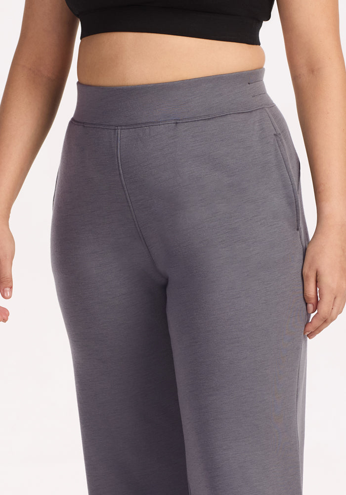 A woman models Woolx Bree Lounge Pants in Arctic Dusk, a relaxed fit, high-waisted gray style, paired with a black crop top. Image shows mid-torso to thighs against a white background.