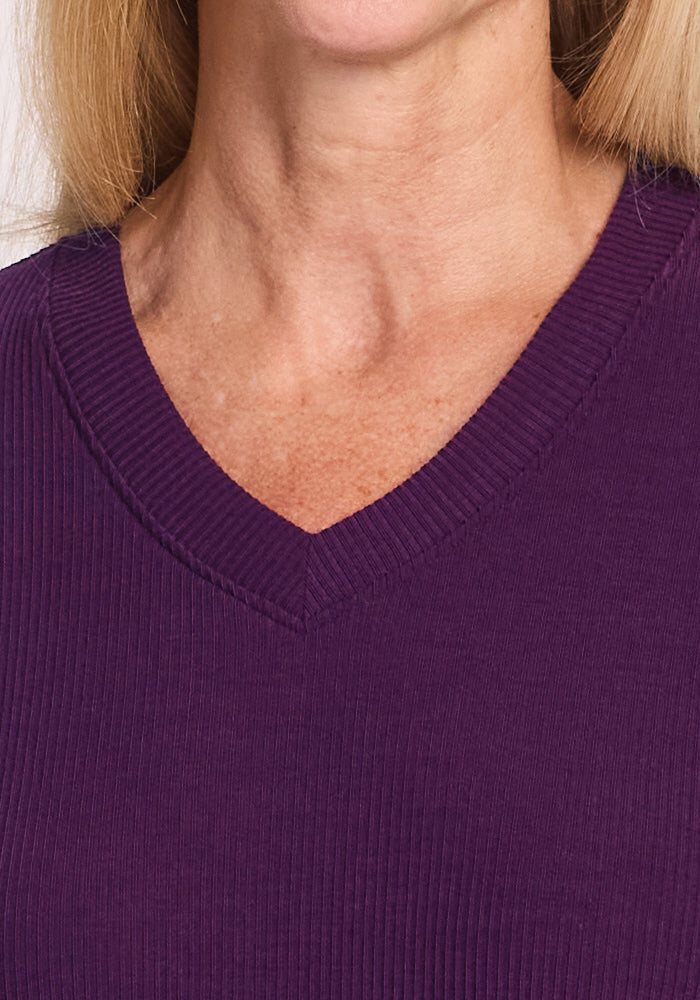 A close-up of a person wearing the Woolx Evie Ribbed Tunic in Majestic Purple, highlighting its V-neckline and upper chest. This cozy Merino wool top is ideal for temperature regulation. Blonde hair frames the edges of the image.