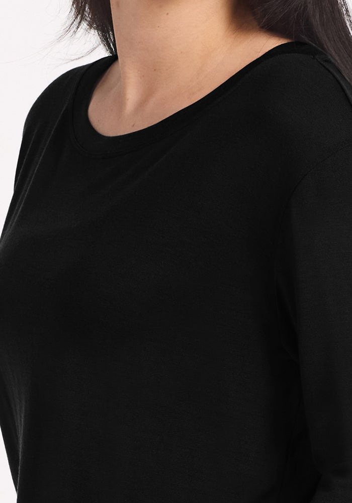 A close-up of a person wearing the Woolx Ashlie Lounge Top in black, showing the chest, shoulder, and part of the neck with long dark hair partially visible. The background is plain white.