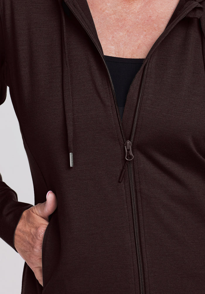 A person wearing the Woolx Ryann Hoodie - French Roast with their left hand in the pocket. The merino wool hoodie is partially unzipped to show a black top underneath—an ideal all-season choice for women's comfort and style.