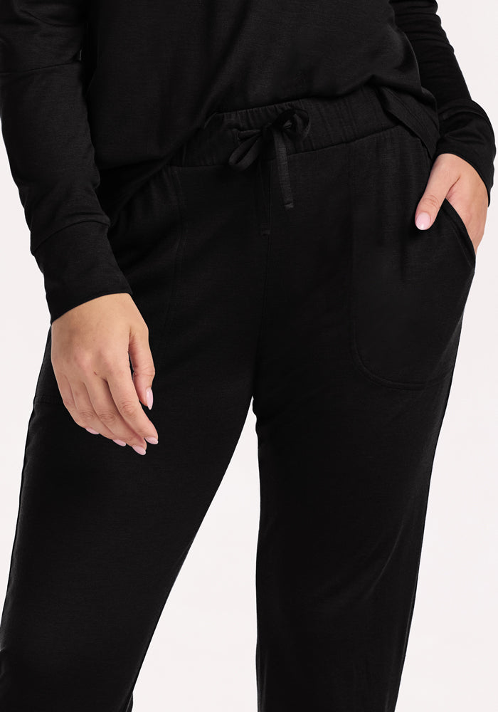 Dressed in Woolx Mary Kate Lounge Pants - Black and a matching long-sleeve top, a person stands against a light background—ideal travel loungewear with moisture-wicking comfort.
