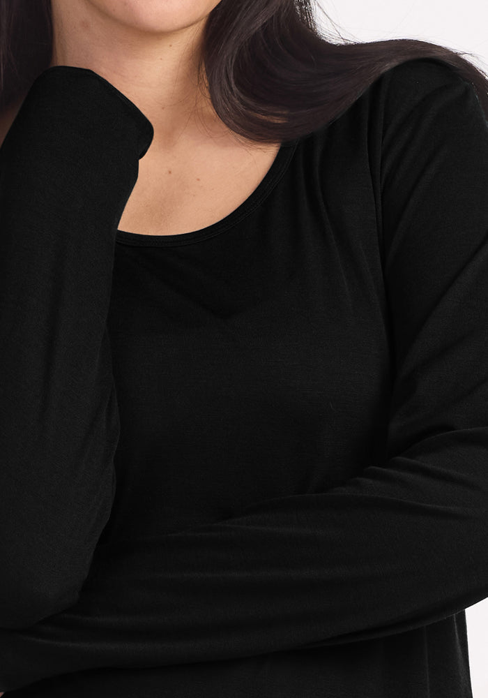 A person with long dark hair wears the Woolx Lucille Long Sleeve Nightgown in black, one arm bent with hand near chin. Only the mouth and chin are partially visible.