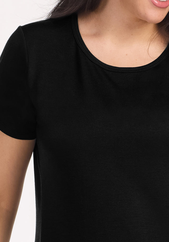 Close-up of a person wearing the Woolx Desi Nightgown in black, featuring a plain Merino wool short-sleeve design. Image shows the upper torso, part of the left arm, neck, and partial smile; head mostly out of frame.