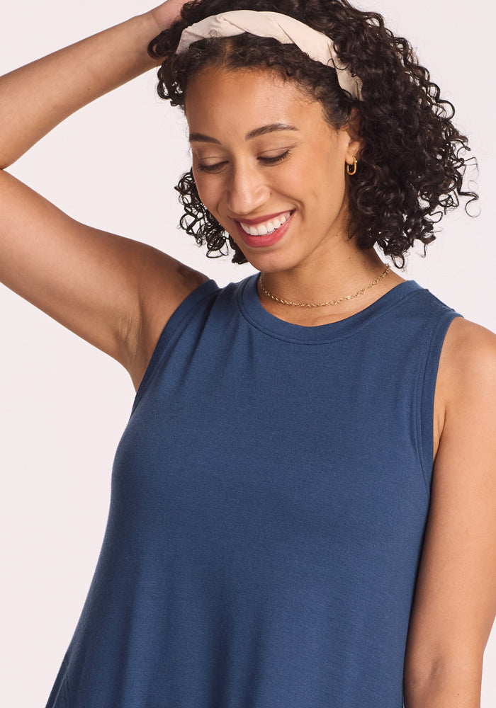 A woman with curly hair and a headband smiles while looking down, wearing the Woolx Clara Dress in Starry Night, resting one hand on her head against a light background.