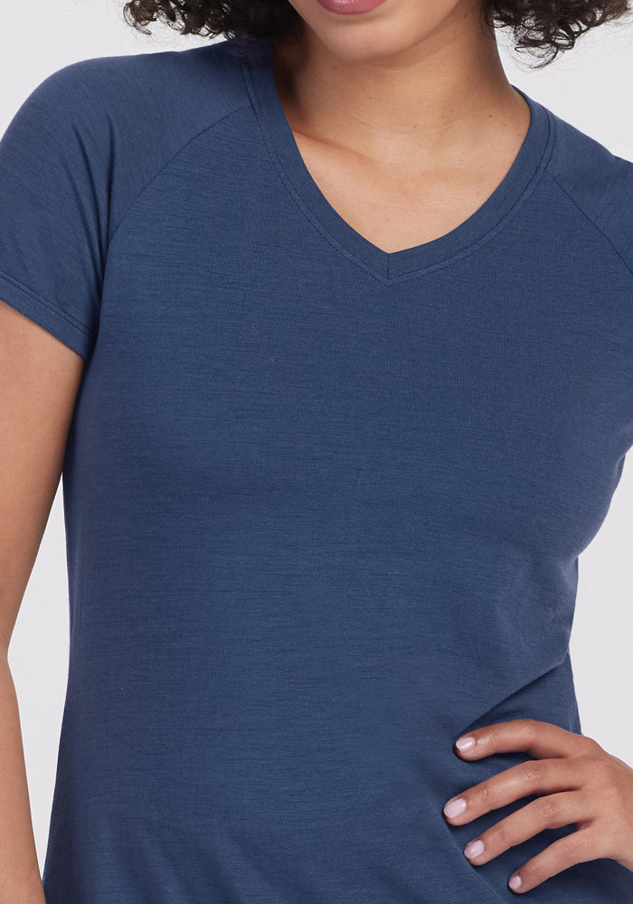 A person wearing the Woolx Mia V Neck in Starry Night, a short-sleeved Merino wool t-shirt, stands with one hand on their hip. The cropped image shows their upper body and part of their face.