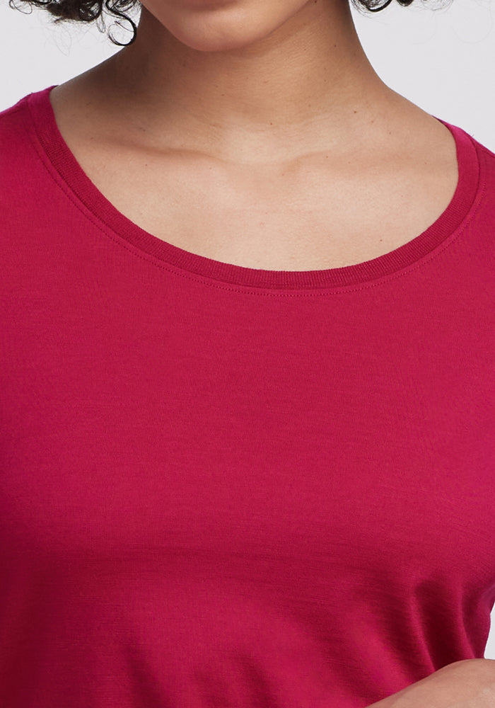 A close-up of a person wearing the Woolx Jenny 3/4 Sleeve Crew Neck in Poppy Spark. Only the lower face, neck, and upper chest are visible. The bright pink Merino wool shirt stands out against a plain light background.
