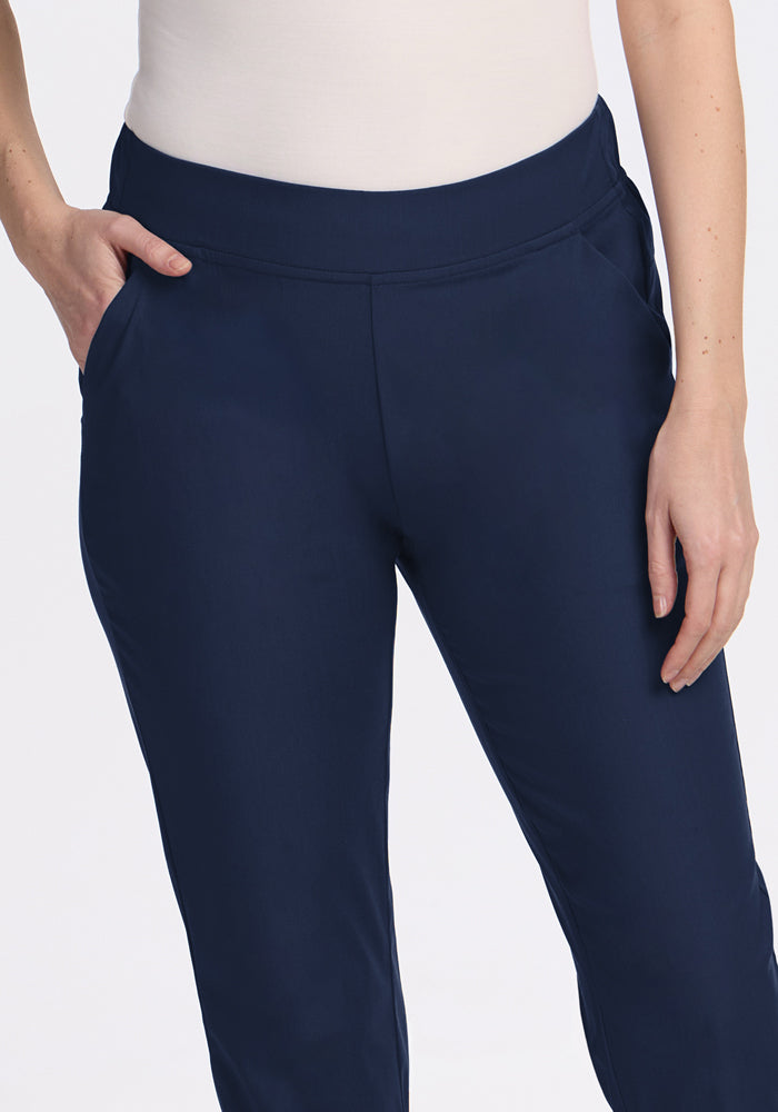 A person wears Woolx Nicole Ankle Pants in Deep Navy with a tapered-leg fit and a white top, standing against a plain white background with one hand in their pocket and the other by their side.