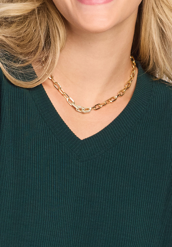 A woman wears the Woolx Evie Ribbed Tunic in Deep Timber and a chunky gold chain necklace with a decorative clasp. Only the lower part of her face, neck, and upper chest are visible.