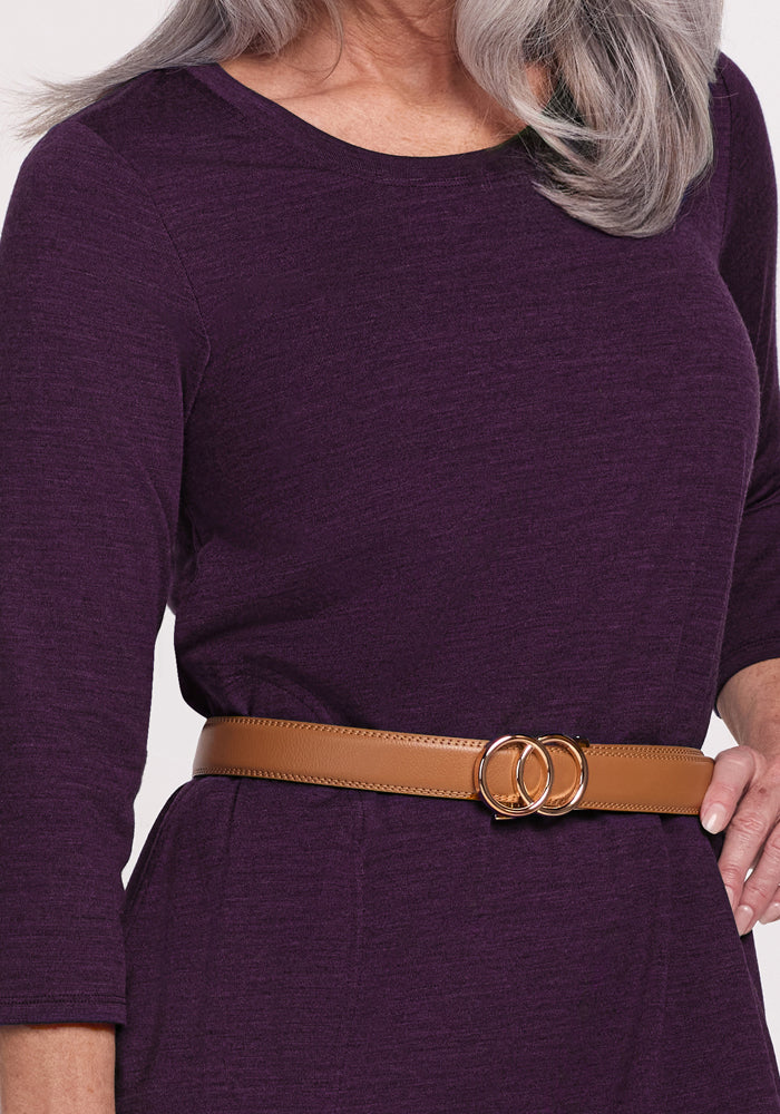 A woman with long gray hair wears the Woolx Rissa A Line Dress in Deep Plum, featuring three-quarter sleeves and a tan belt with two interlocking gold rings. Perfect for fall and winter, only her torso and part of her left hand are visible.