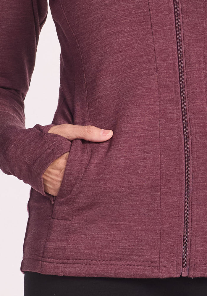 A person wearing the Woolx Finley Zip Up Sweatshirt in Grape Harvest Melange with their left hand partially in the pocket. The odor-resistant sweatshirt features thumbholes and is paired with black pants.