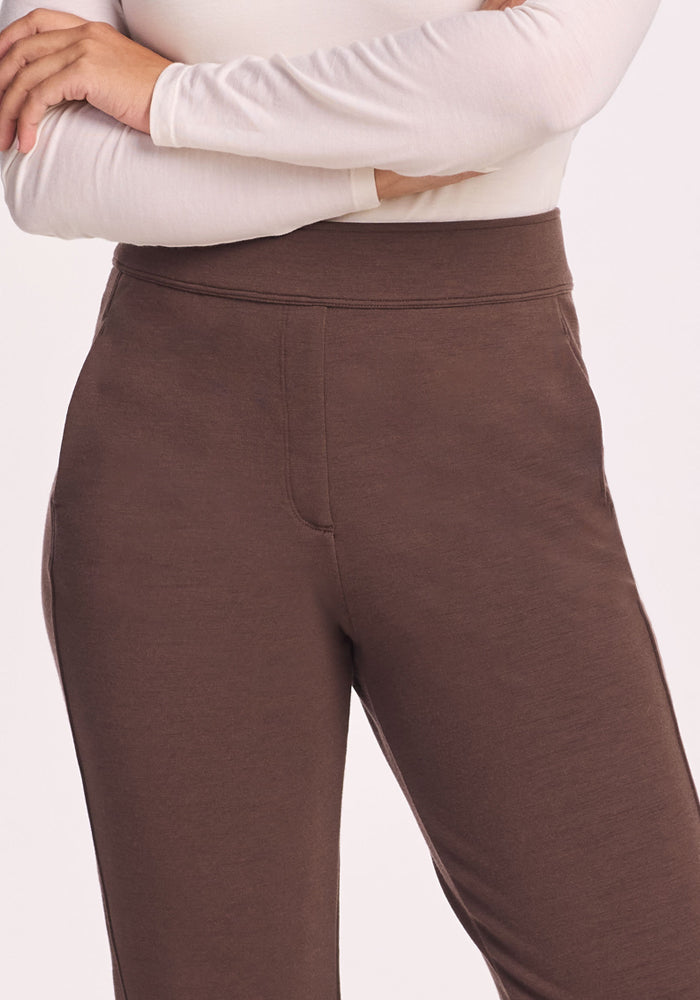 A person stands with arms crossed, their torso and upper legs visible, wearing the Woolx Emerson Straight Leg Pants in Bracken against a plain background.