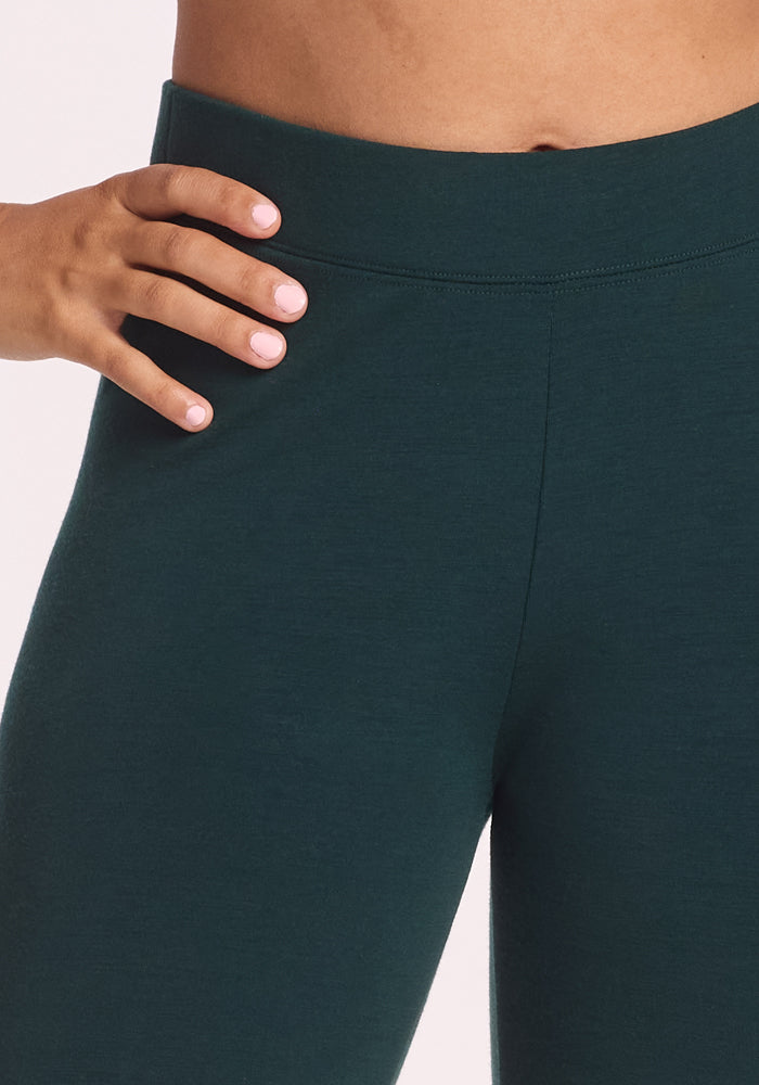 A close-up of a person wearing Woolx's Stella Leggings in Deep Timber, with their left hand on their hip, revealing part of their bare midriff and neatly manicured nails.
