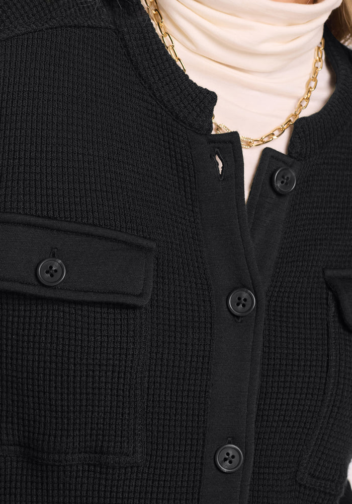Close-up of Woolx Oaklynn Petite Waffle Shacket in black with flap pockets, buttons, and gold chain over cream turtleneck.
