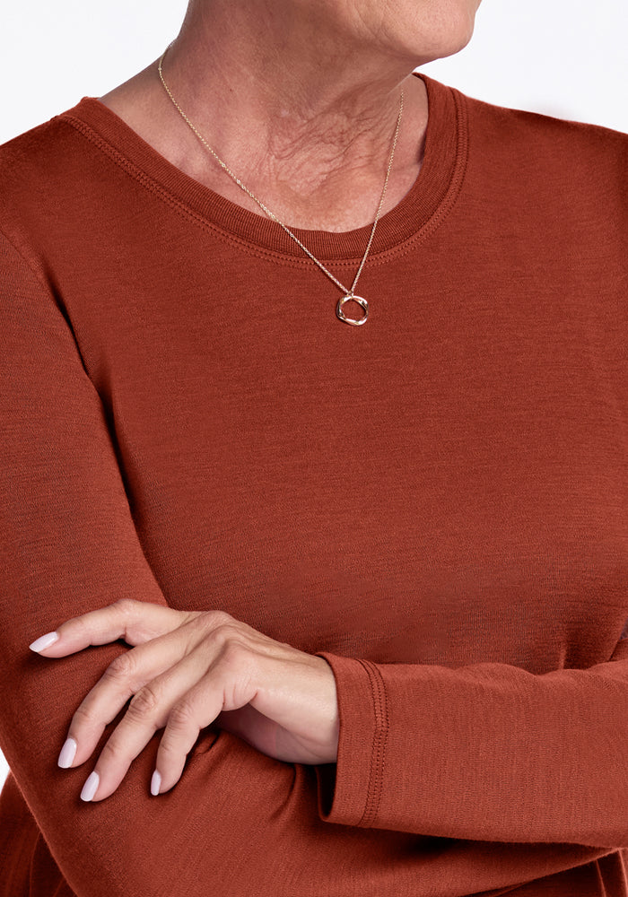 A person wearing the Woolx Blair Tunic in Maple Leaf and a gold necklace with a circular pendant, arms crossed, with only their lower face and upper torso visible.