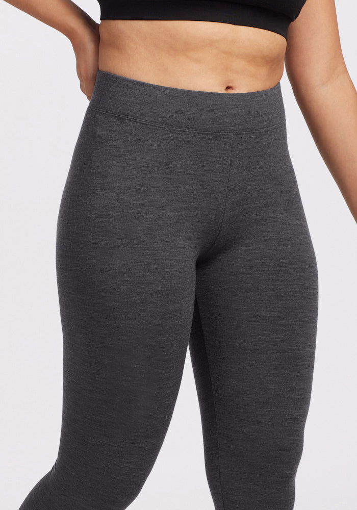 Model wears Woolx Stella Tall - Cinder Melange leggings and a black crop top, hand on hip against plain background.