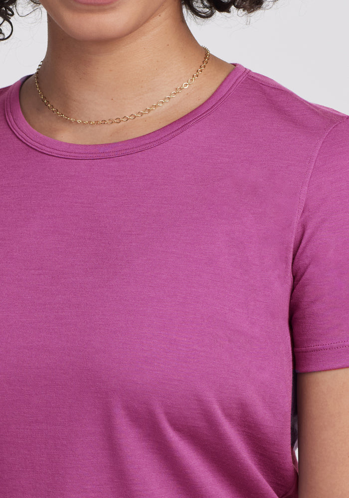 A person wearing the Woolx Liza Crew Neck Tee in Purple Wine and a thin gold chain necklace, shown from shoulders to just above the chest against a plain, light-colored background.