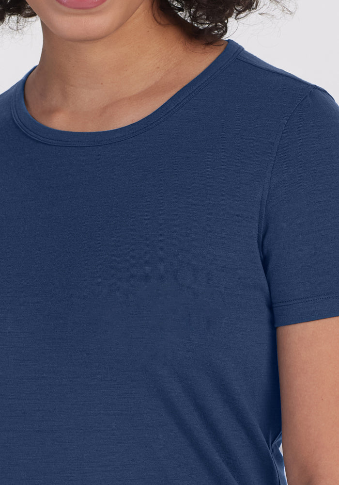 A person is shown from the shoulders up wearing the Woolx Liza Crew Neck Tee in Starry Night, with part of their face and curly hair visible.