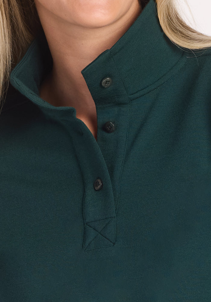 Close-up of a person wearing the Woolx Annie 3 Button Pullover in Deep Timber, with three black buttons undone. The soft merino wool fabric flatters their light skin and blonde hair, which are partially visible in the shot.