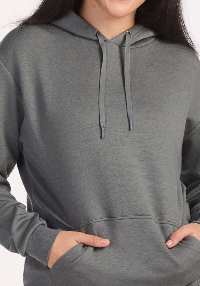 A person wearing the Woolx Avery Hoodie in Sedona Sage, with one hand in the front pocket, is shown from neck to waist against a plain background.