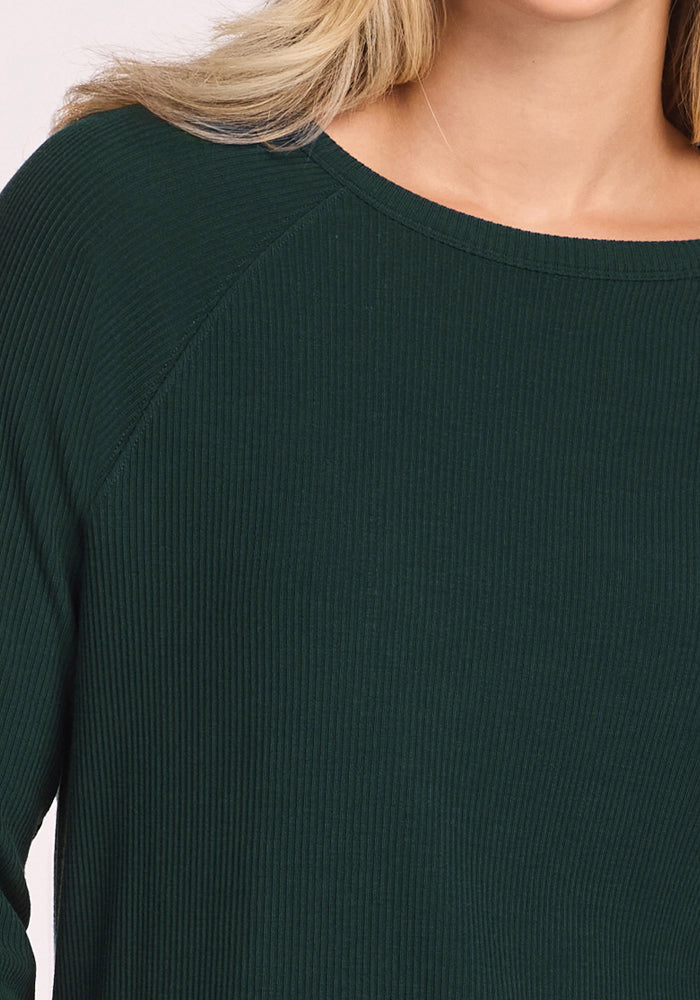 A close-up shows a person in the Woolx Ainsley Sweater - Deep Timber, revealing only the lower face, neck, and upper torso. The blonde hair is partially visible. This ribbed women’s top combines temperature regulation with style and comfort.