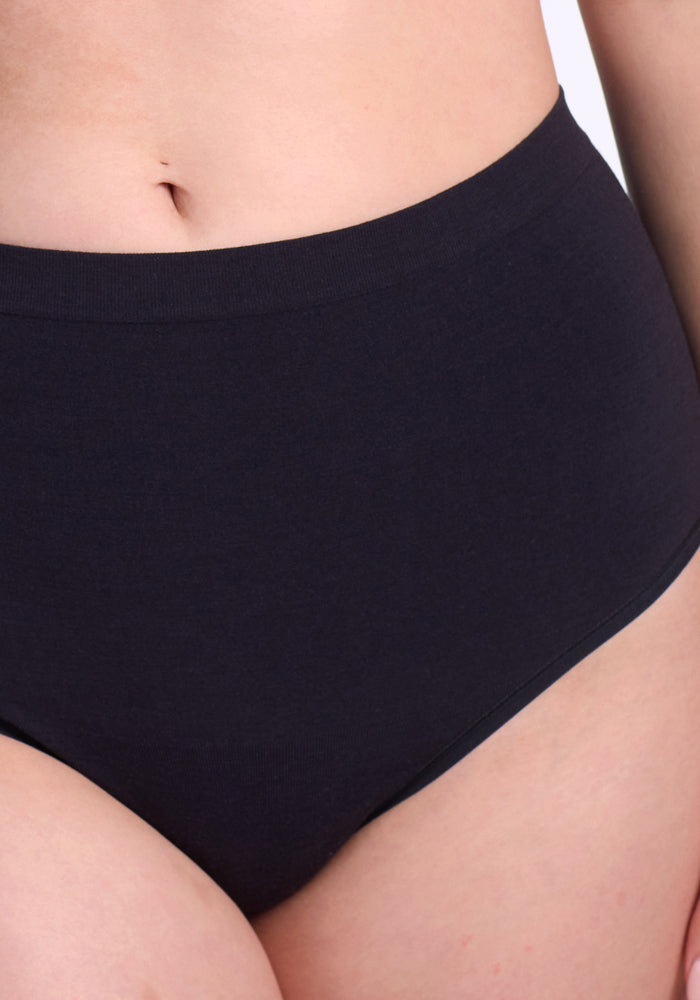 A close-up of a person wearing Woolx Mabel Full Coverage Underwear in black, showcasing the high-waisted, seamless design for comfort. Only the midsection and upper thighs appear against a plain background.