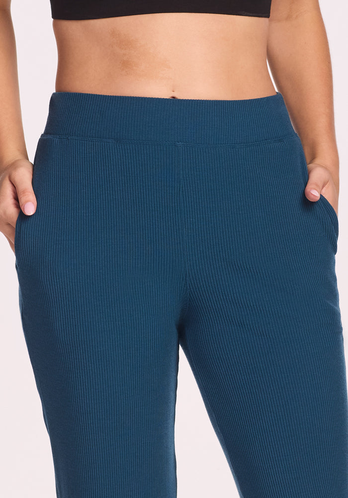 A person wears Woolx's Luca Ribbed Pants in Majolica Blue, shown from mid-torso to mid-thigh with hands in pockets against a plain background.