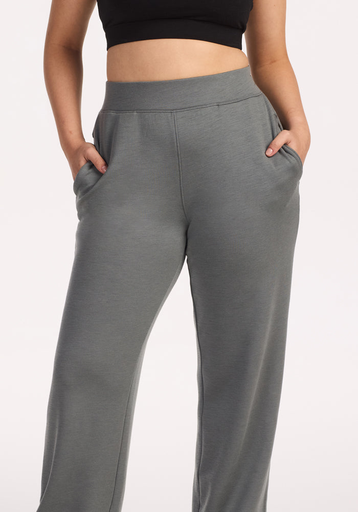 A person wearing Woolx Bree Lounge Pants in Sedona Sage, high-waisted and loose-fitting with hands in pockets, paired with a black crop top. The background is plain white.