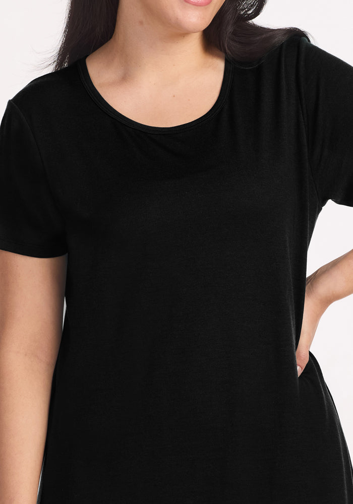 A woman in a plain black short-sleeve t-shirt stands with one hand on her hip against a white background, showcasing the Woolx Desi Nightgown—perfect for layering over temperature-regulating sleepwear. Her face is partially out of frame.