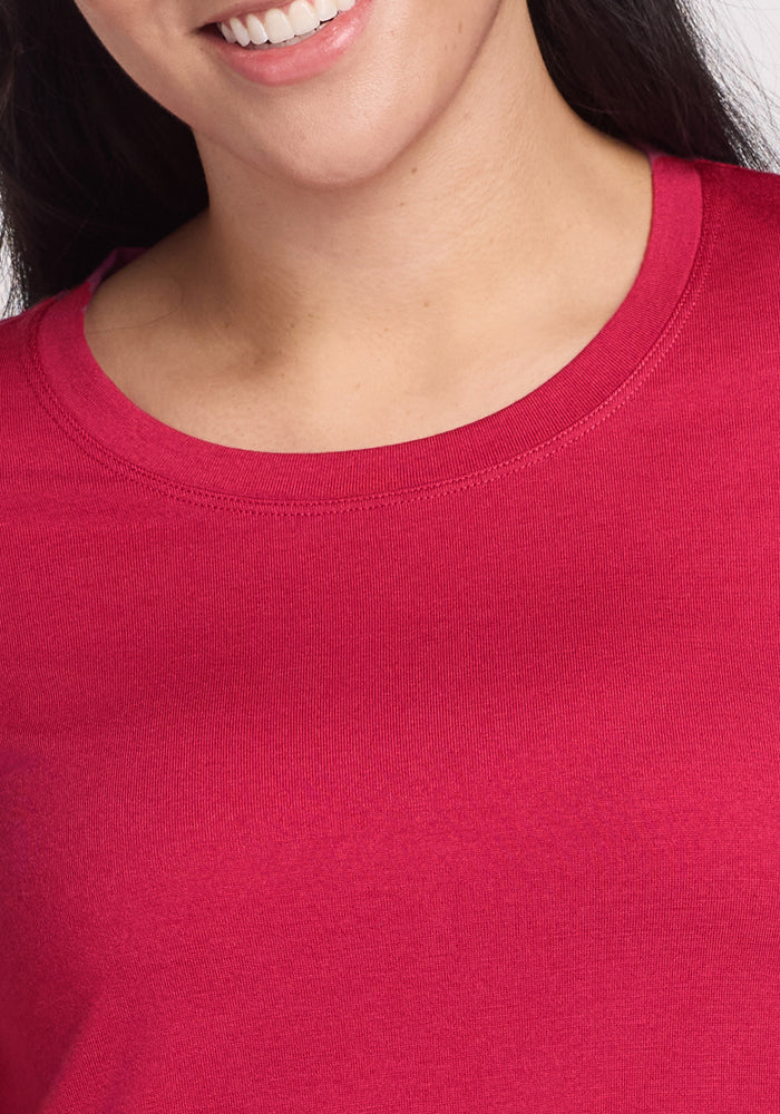 A close-up of a person smiling, showing the lower half of their face and neck, wearing the Woolx Rissa A Line Dress in Poppy Spark—a bright pink Merino wool dress ideal for travel.