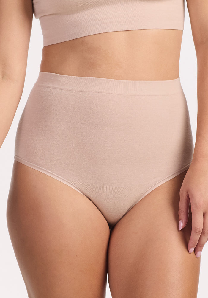 A person wears Woolx's Mabel Full Coverage Underwear in Sand and a matching crop top, both featuring seamless comfort, shown from shoulders to upper thighs against a plain background.