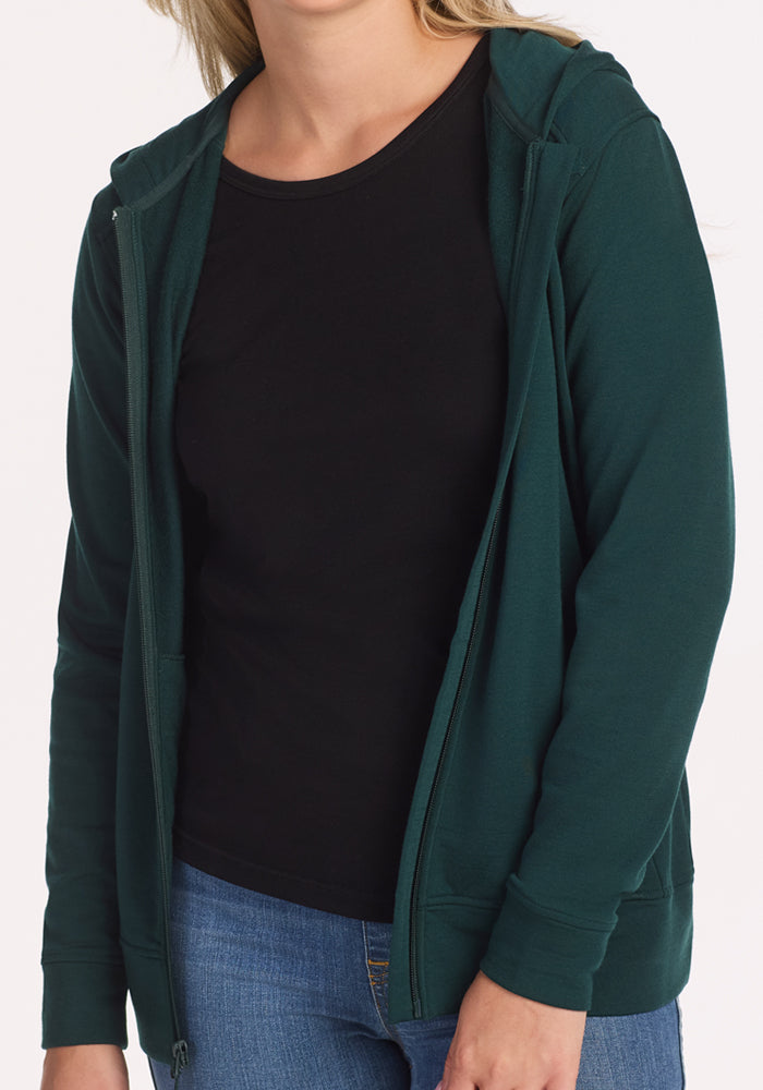 A person in the Woolx Darby Zip Up Hoodie in Deep Timber, layered over a black t-shirt and blue jeans, stands against a plain white background with their face partially out of frame.