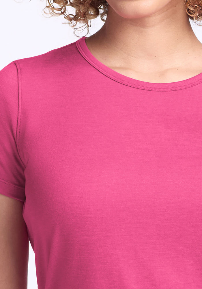 A person with curly hair is wearing the Woolx Liza Crew Neck Tee in Raspberry Fizz. Only the lower part of their face, neck, shoulder, and upper torso are visible.