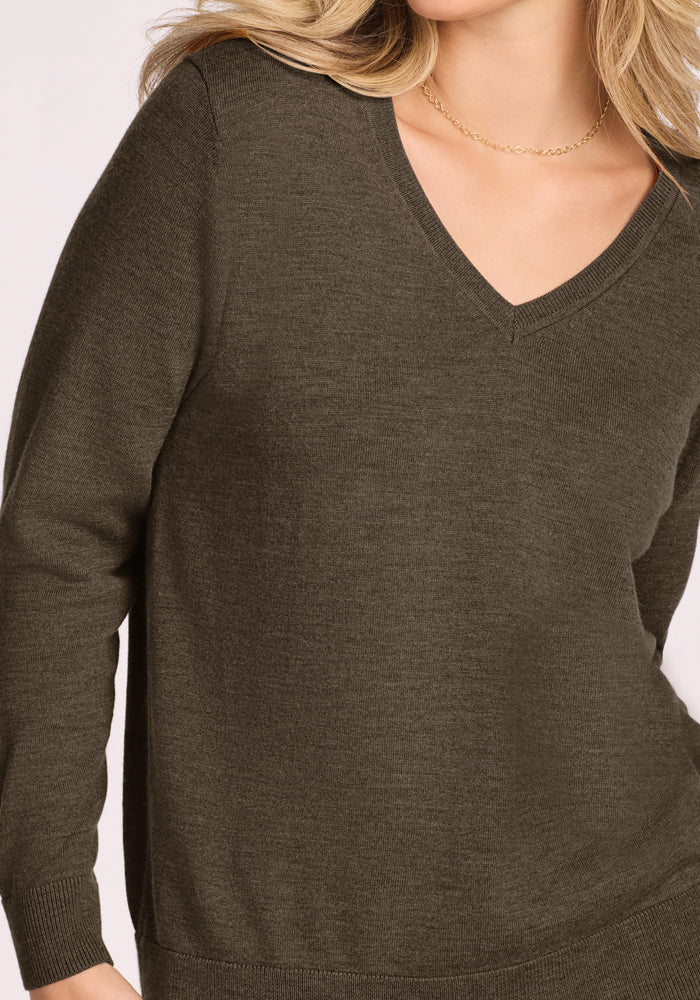 A woman wearing the Woolx Francesca Sweater in Pine Needle, a long-sleeve Merino wool V-neck, paired with a delicate chain necklace and wavy blonde hair, shown from shoulders to hips.